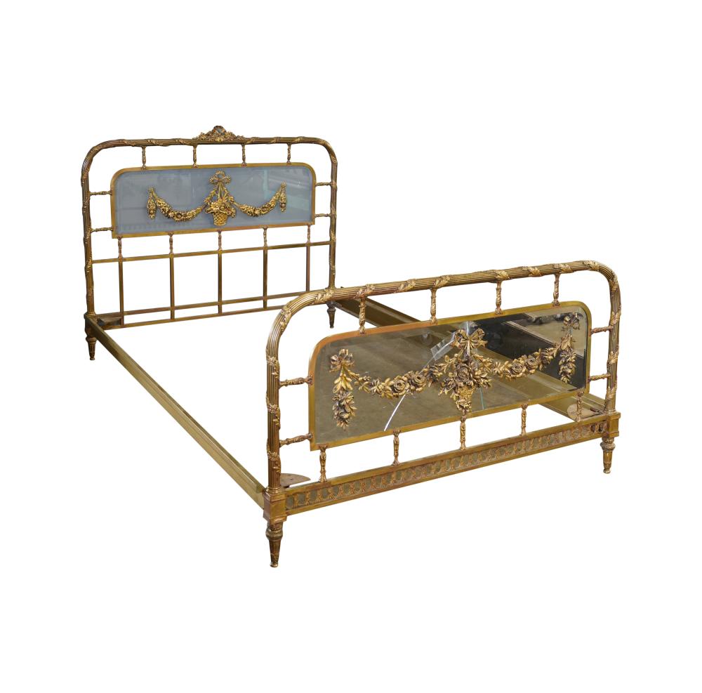 Gilt metal bed frame with arched headboard and clear glass panels, featuring ornate floral finials.