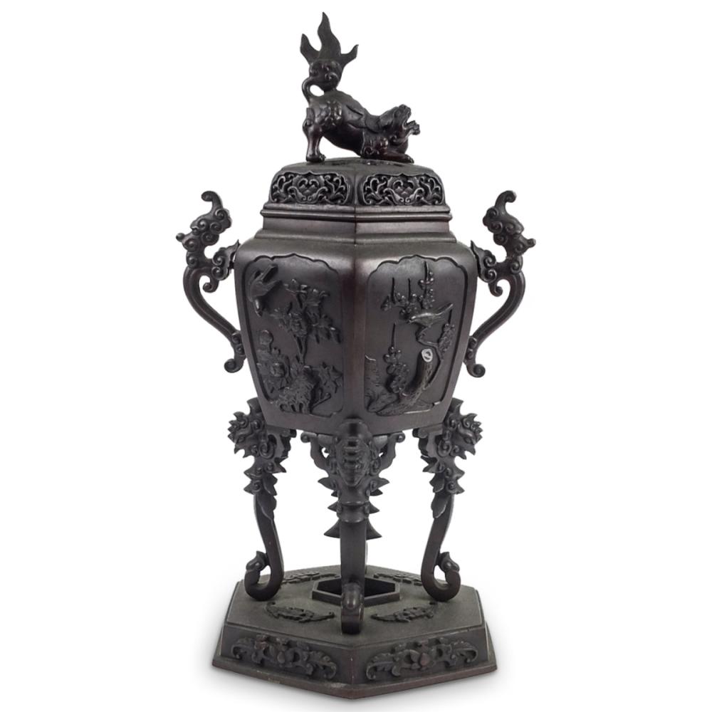 Metal incense burner with ornate handle-like supports, hinged panels, and a dragon finial on top, photographed on a white background.