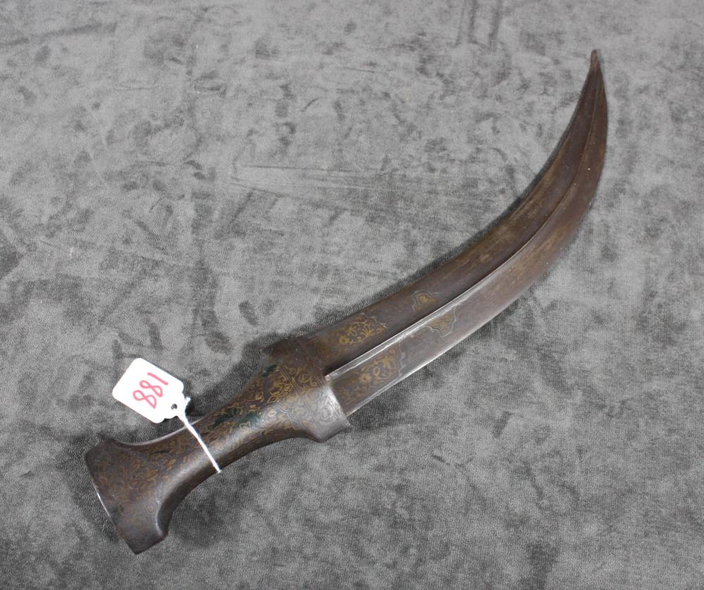 Close-up of a curved dagger with a decorated wooden handle and patterned metal blade laid on a gray surface.