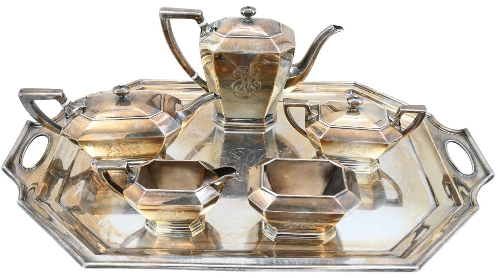 Five-piece silver-colored tea set with a teapot, covered sugar bowl, creamer, and two serving pieces on a matching tray.