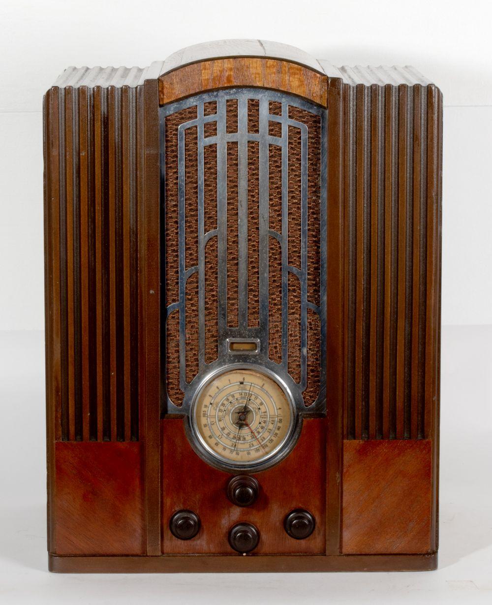 Front view of a vintage wooden front radio with chrome grille, arched dial window, and round clock-style tuning dial.