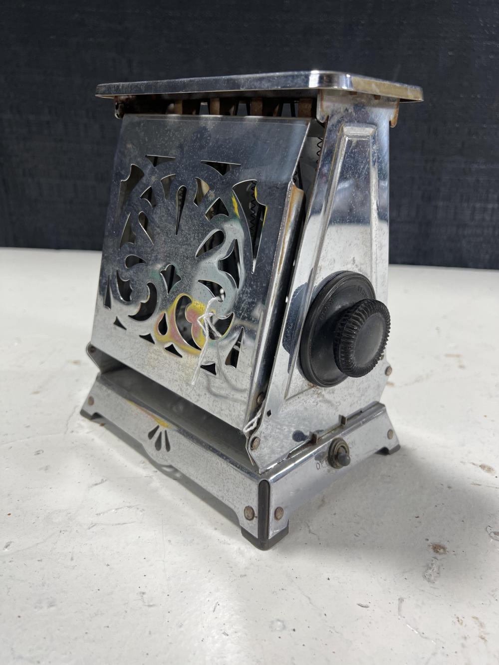 Chrome toaster with a metal crumb tray and vented sides, standing on a tabletop against a dark background.