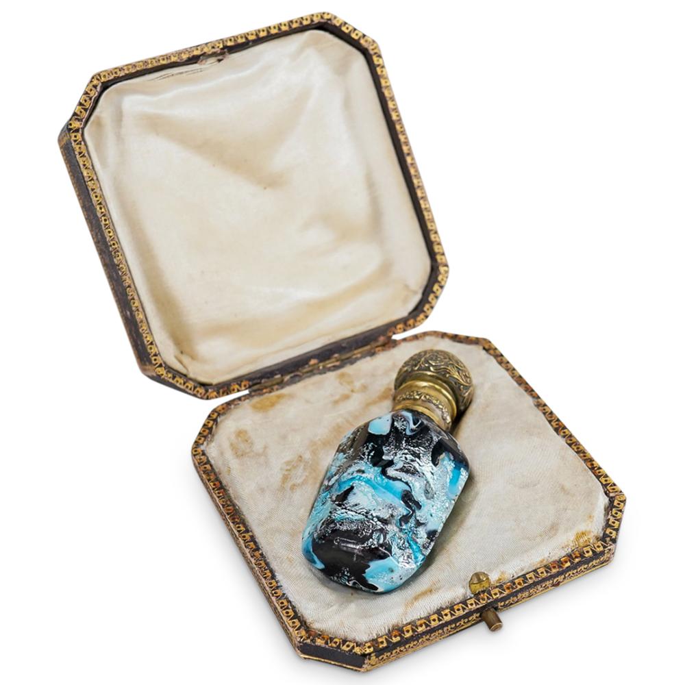 Antique-style perfume bottle with a gold-toned ornate cap inside an open hexagonal presentation box with velvet lining.