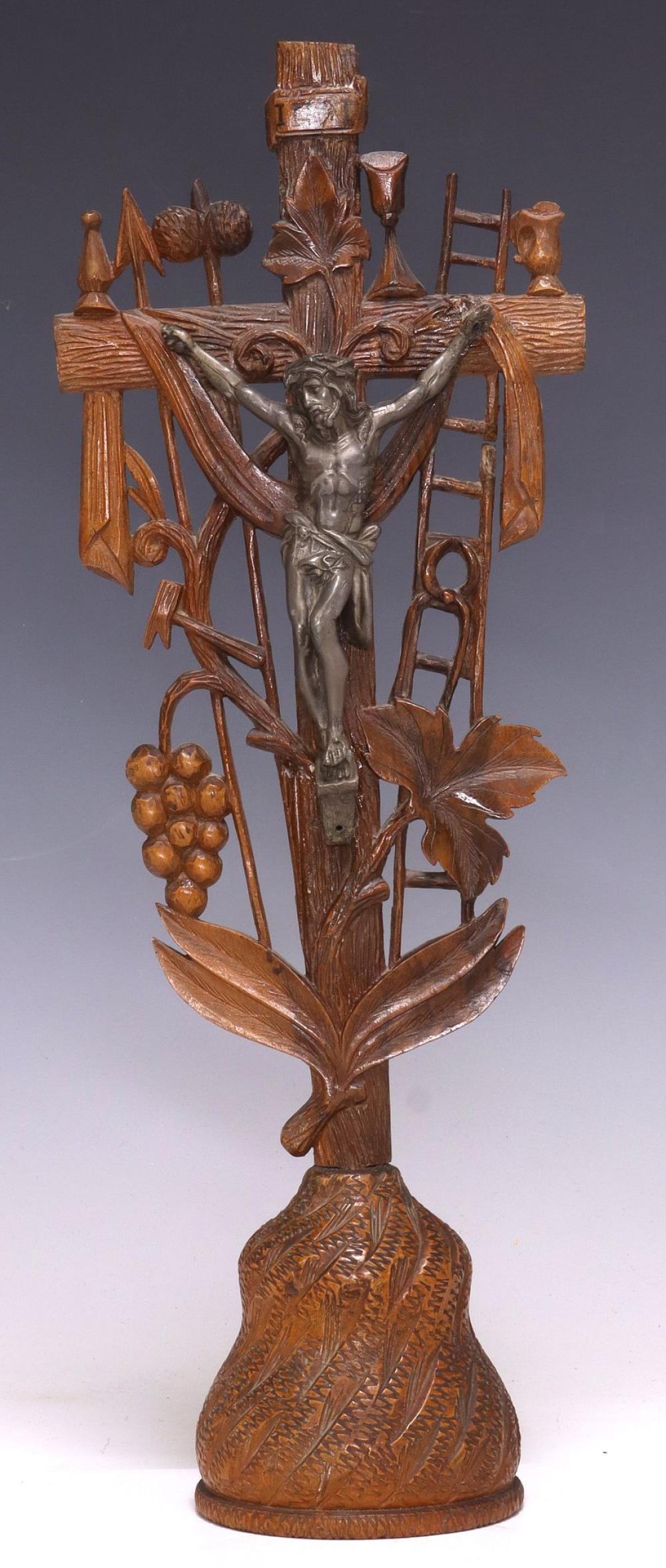 Carved wood and metal crucifix featuring a central figure of Jesus with outstretched arms surrounded by decorative leaves, grapes, and finials.