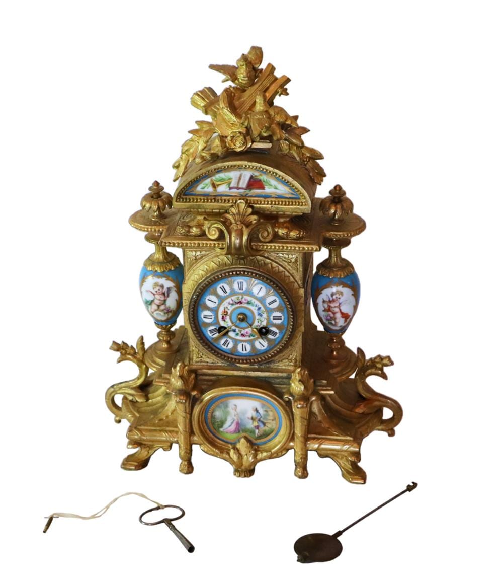 Gilded French-style mantel clock with decorative blue-and-white painted panels and a floral crest on top, showing an ornate clock face and hands.