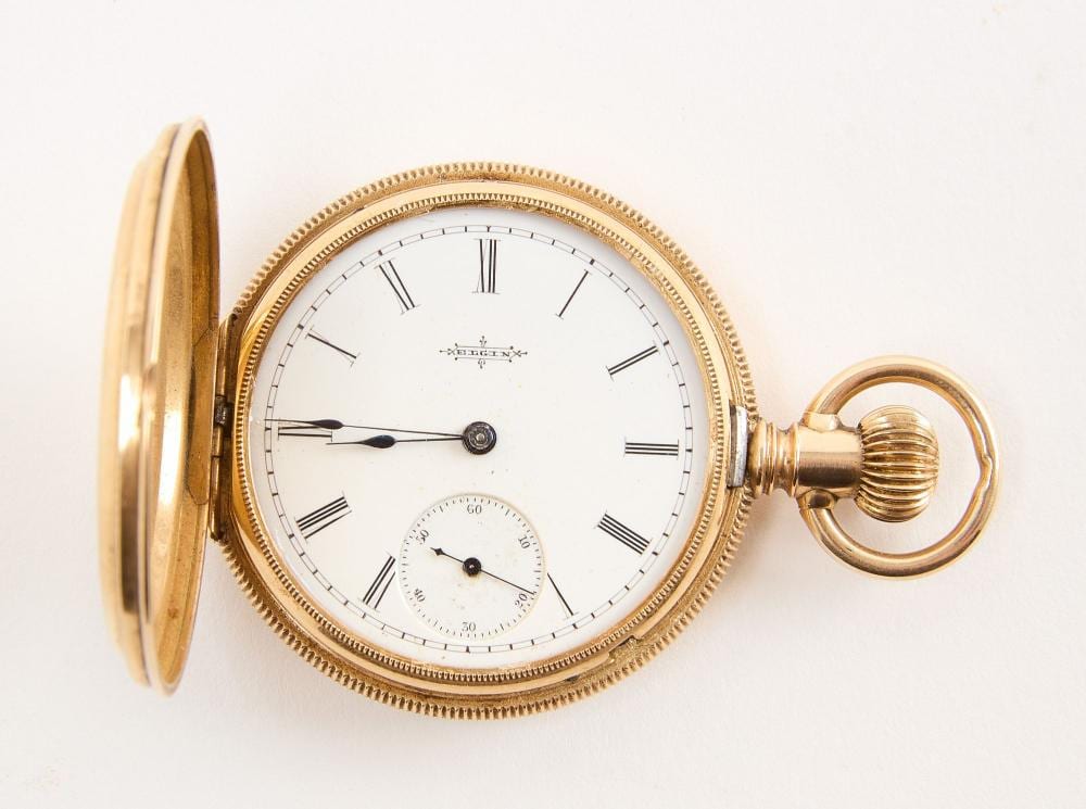 Open-faced gold pocket watch with roman-numeral dial, central hands, and a secondary seconds subdial, with the case back tilted open.