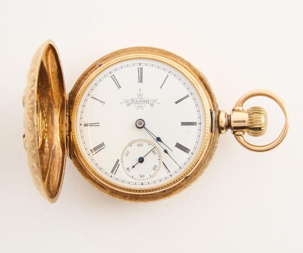 Gold-colored open-faced pocket watch with white dial, Roman numerals, blue hands, and an open hinged cover showing the interior