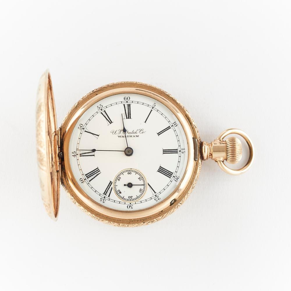 Open-face gold tone pocket watch with white dial, Roman numerals, and a small seconds subdial, shown with the hinged cover open.