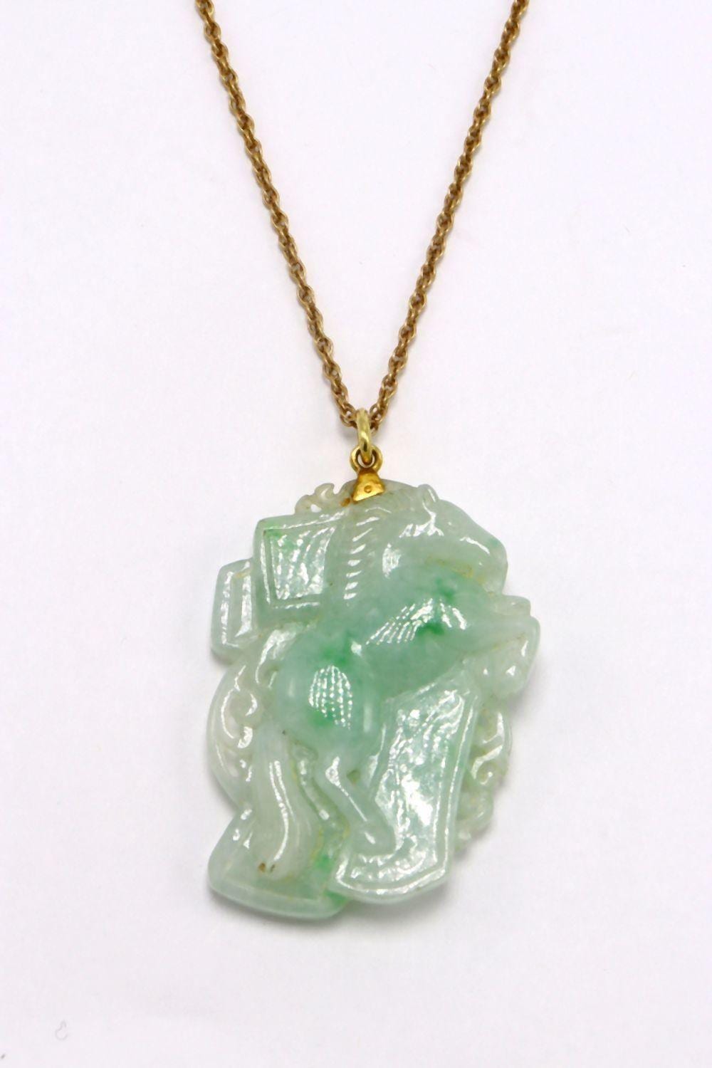 Gold chain necklace with a green carved pendant shaped like a seated figure.