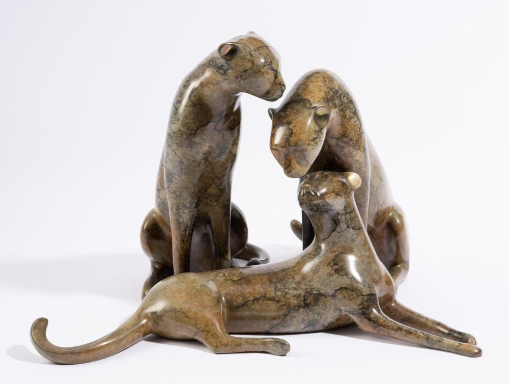 Bronze-toned cheetah sculpture: two cheetahs upright facing each other over a reclining cheetah on a plain white background.