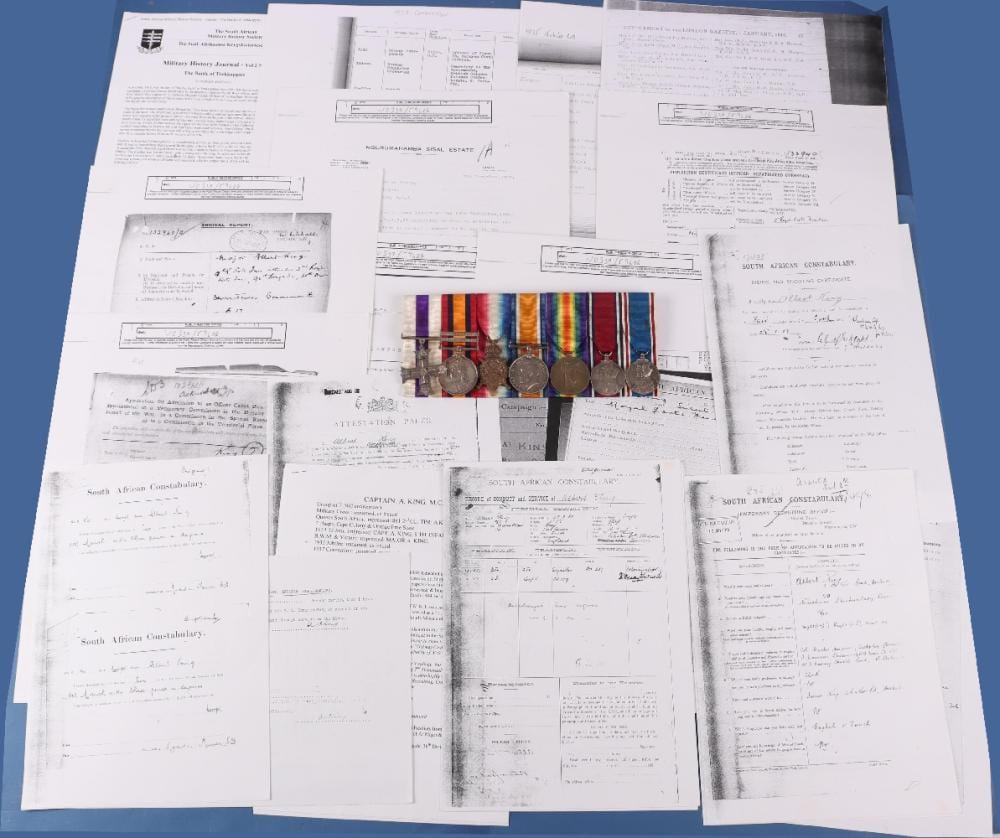 A spread of official documents and papers with a row of colorful medals and several metal medal medallions on top.