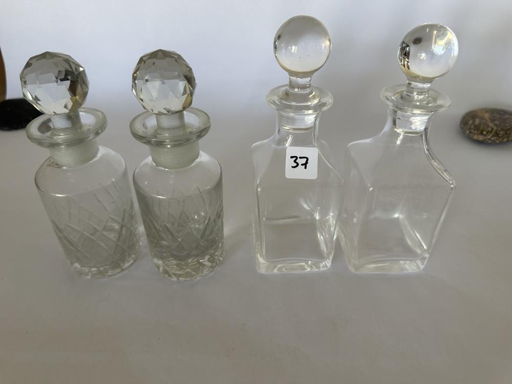 Two clear glass decanters with faceted stoppers, photographed on a light background.