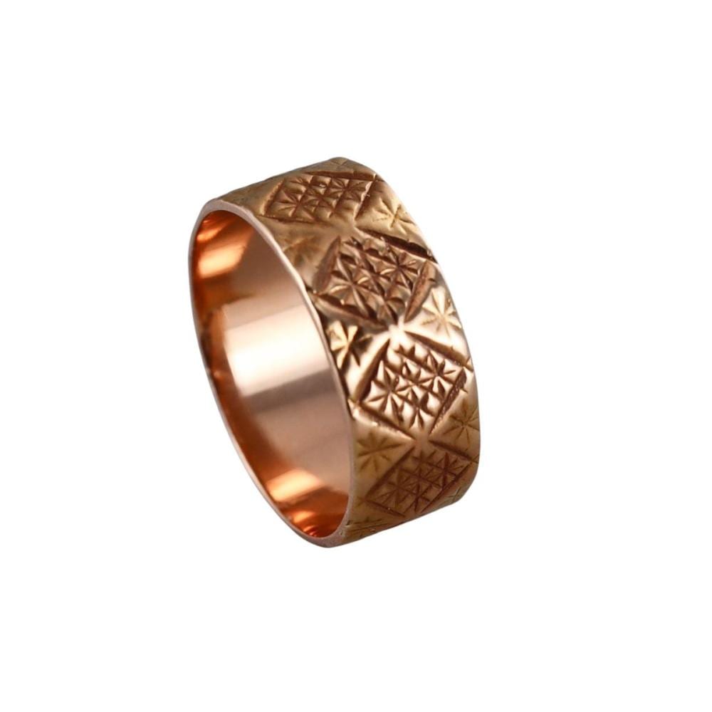Close-up of a gold-colored wedding band ring with textured diamond and starburst engravings on the outer surface.