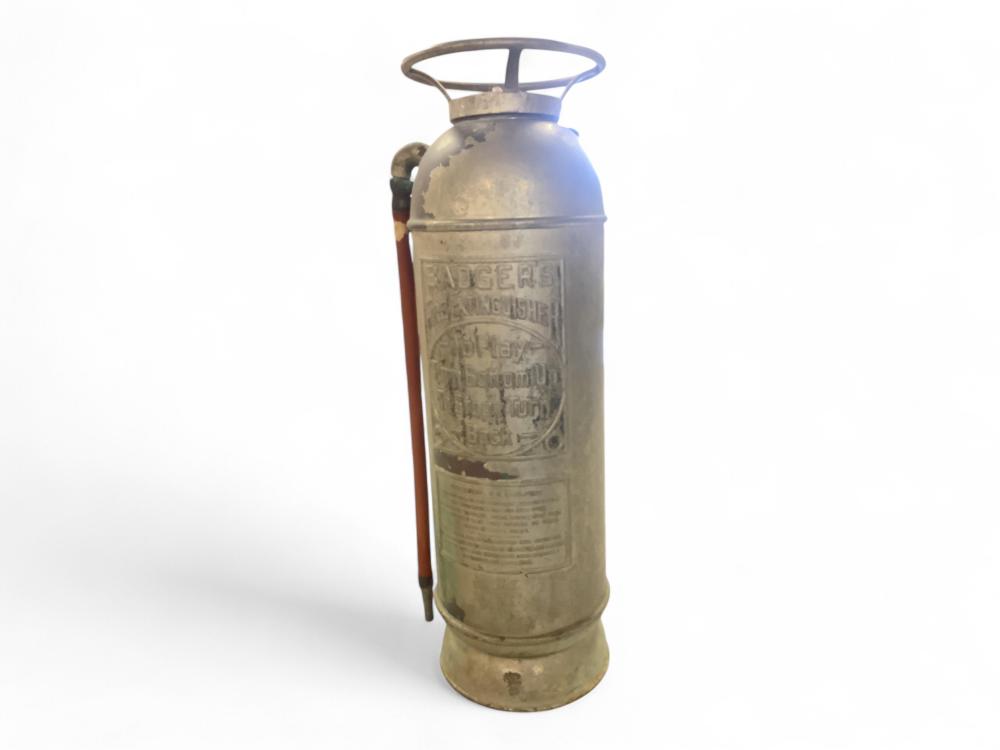 Brass or copper fire extinguisher cylinder with a ring handle and label, shown standing against a white background.