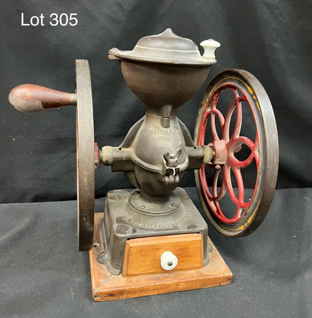 Antique-style hand coffee grinder with metal hopper, crank handle, and red flywheel on a wooden base.