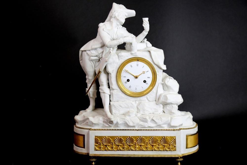 White bisque-style mantel clock with a seated male figure and an inset round clock face framed by gold trim on a decorated base.