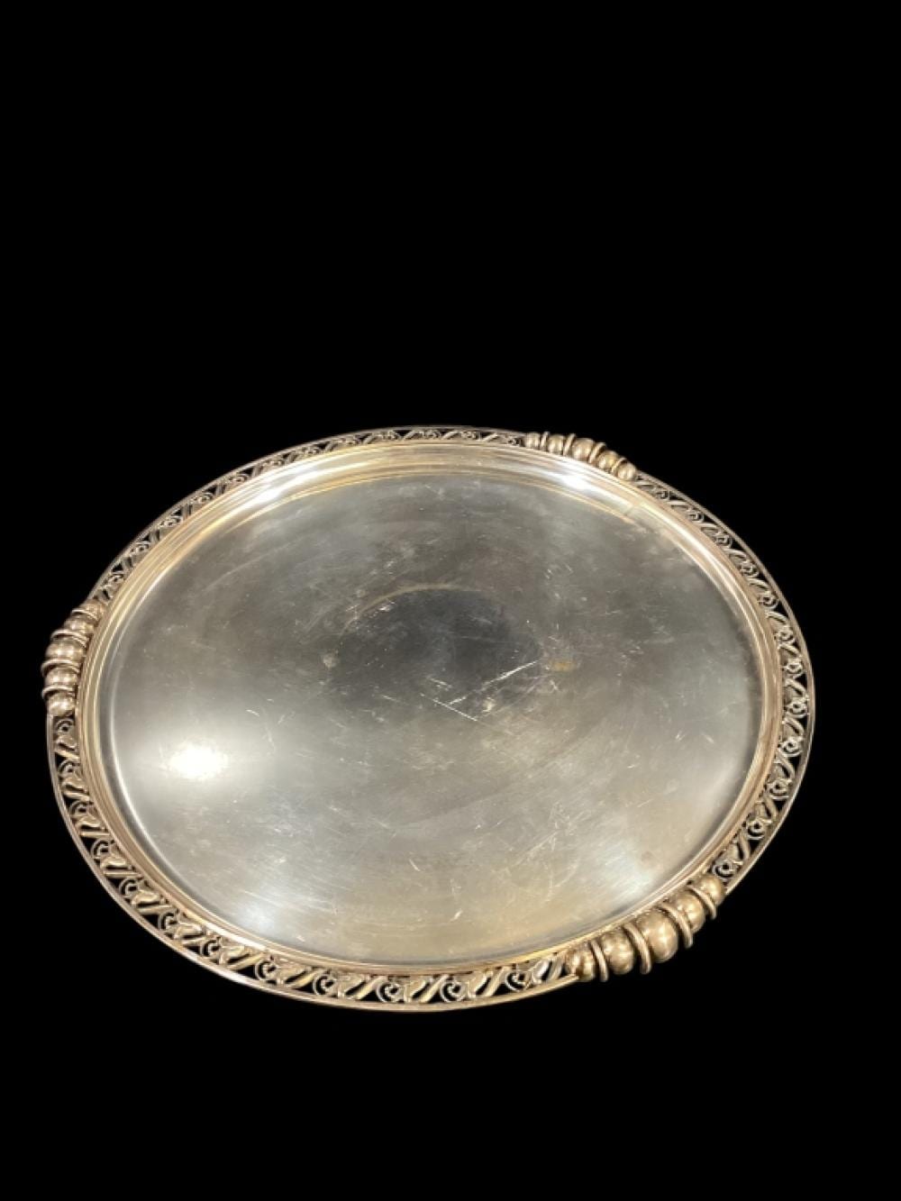 Oval silver-colored serving tray with ornate pierced border and beaded rim, photographed against a black background.