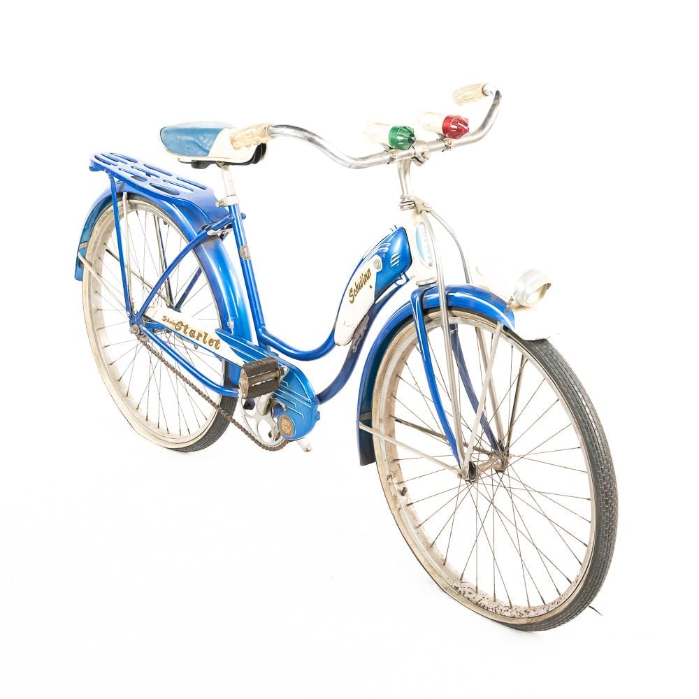 Blue vintage balloon bicycle with chrome handlebars and headlight, white seat and fenders, and spoked wheels.