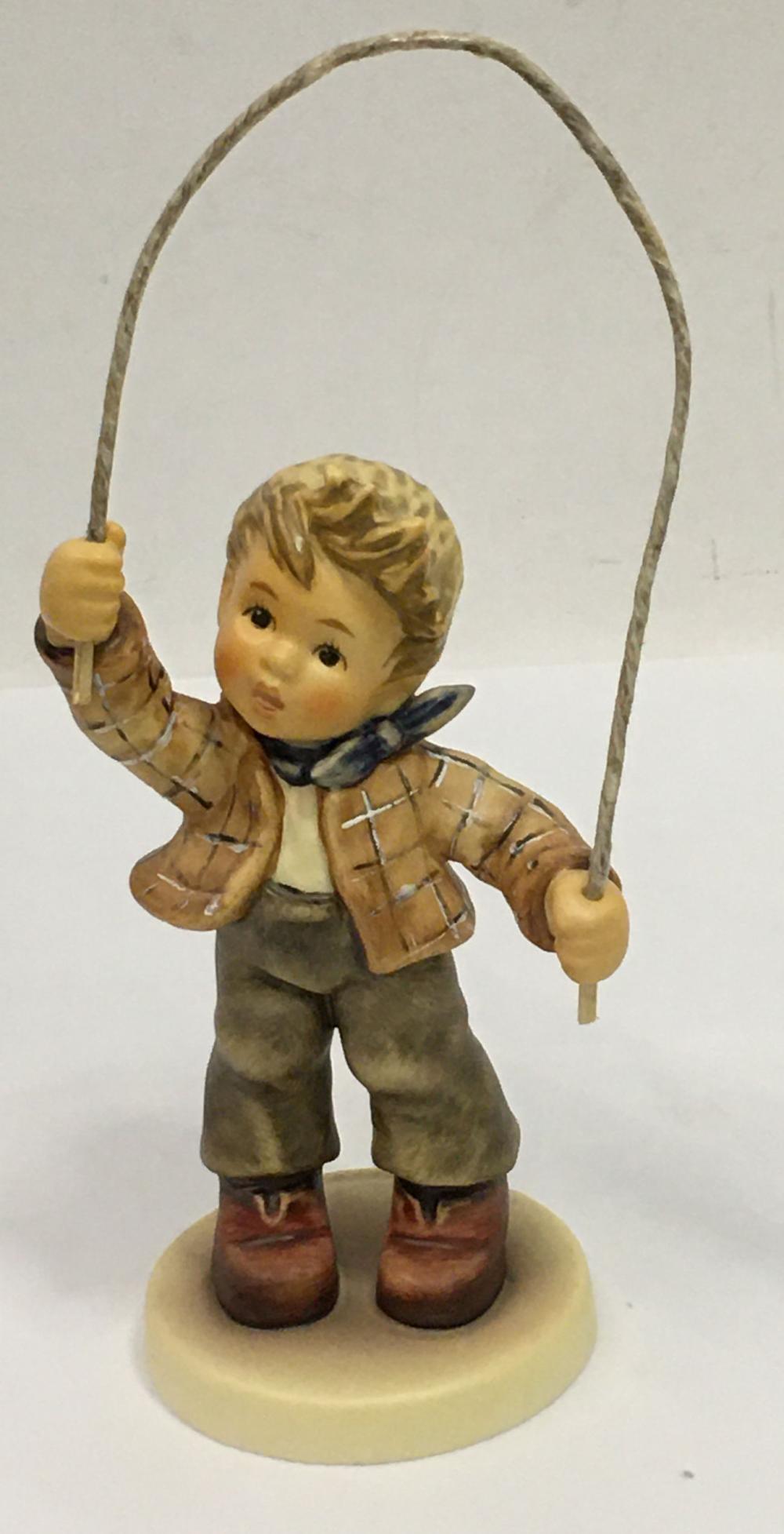 Ceramic figurine of a blond boy holding a small club or staff, with a large halo-like loop above him.