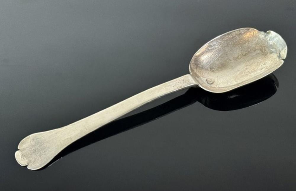 Close-up of a polished metal spoon with an oval bowl and rounded handle on a dark background.