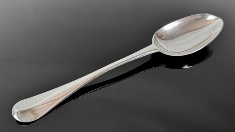 Close-up of a polished silver spoon with an oval bowl and long handle on a dark background.