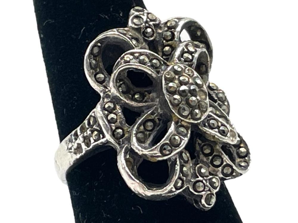 Close-up of a silver-tone decorative ring with dark stones and small round accents on an oval black display.