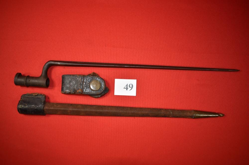 Two bayonet knives laid on a red background, showing their long metal blades and dark black scabbard or handle sections.