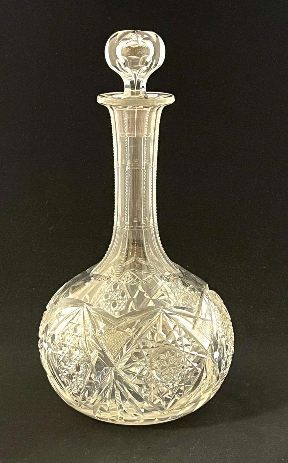 Clear cut-glass decanter bottle with a flared neck and faceted diamond pattern on the body, photographed against a dark background.