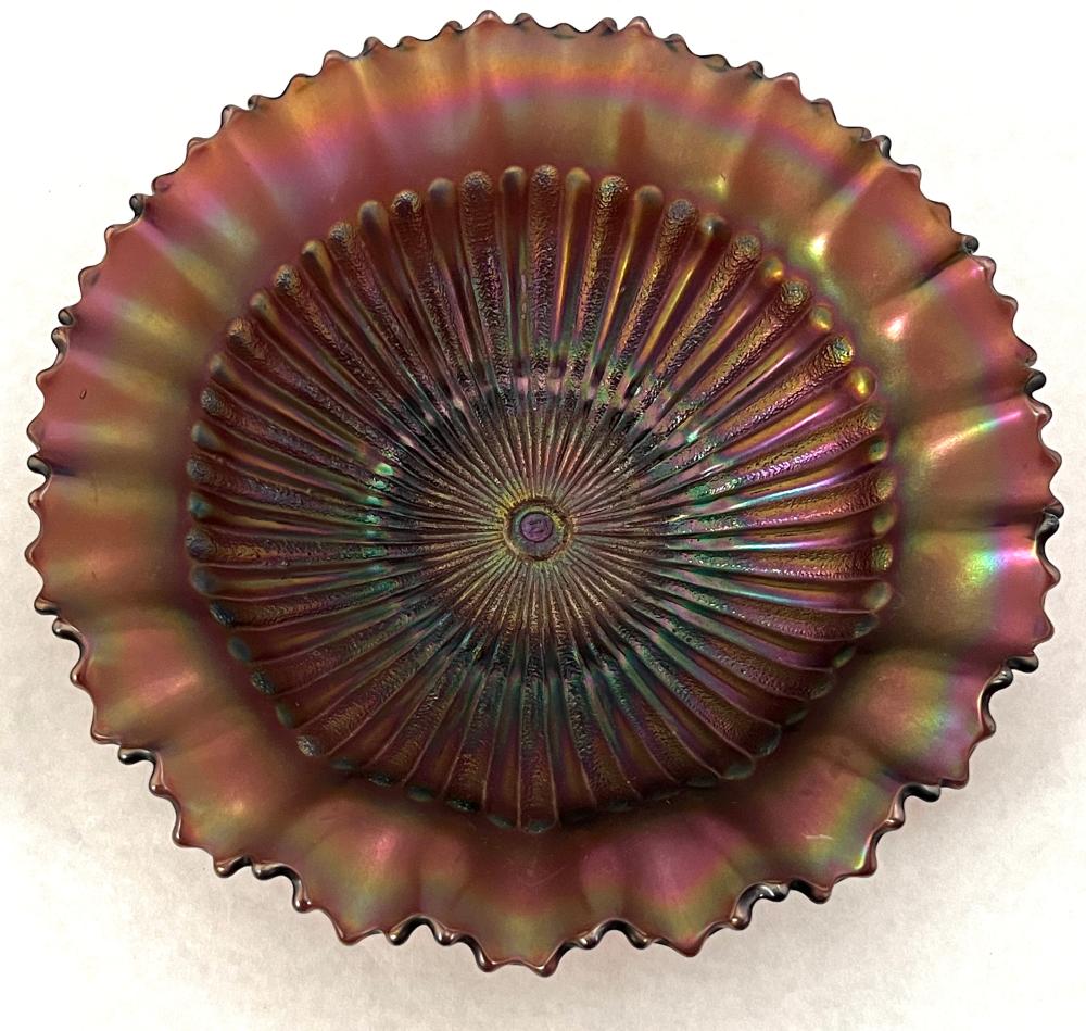Iridescent carnival glass plate with ruffled rim and radial fan pattern in purple and amber tones.