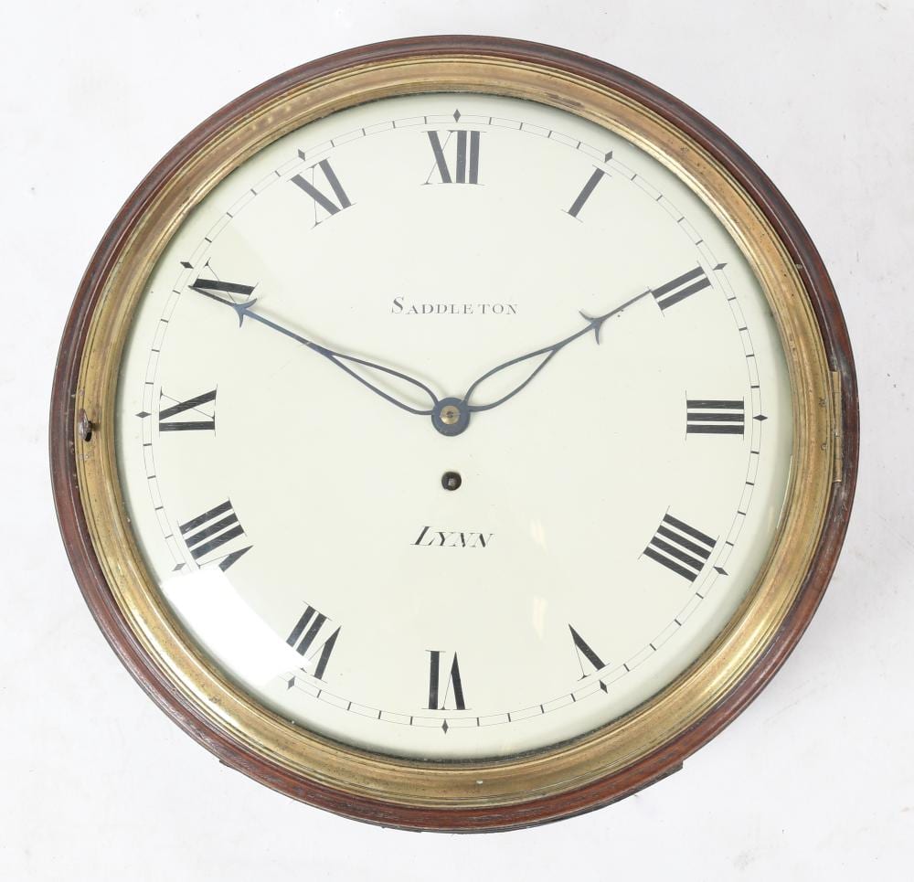 Close-up of a round wall clock face with Roman numeral hour marks, black hands, and gold and brown decorative frame.
