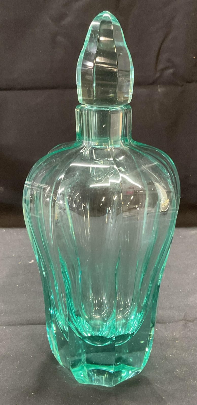 Turquoise cut glass decanter with faceted body and matching stopper against a dark background.