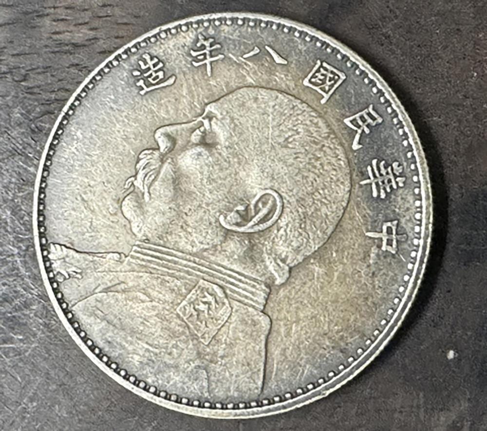 Close-up of a round Chinese-style silver coin with a bearded figure and Chinese characters around the rim.