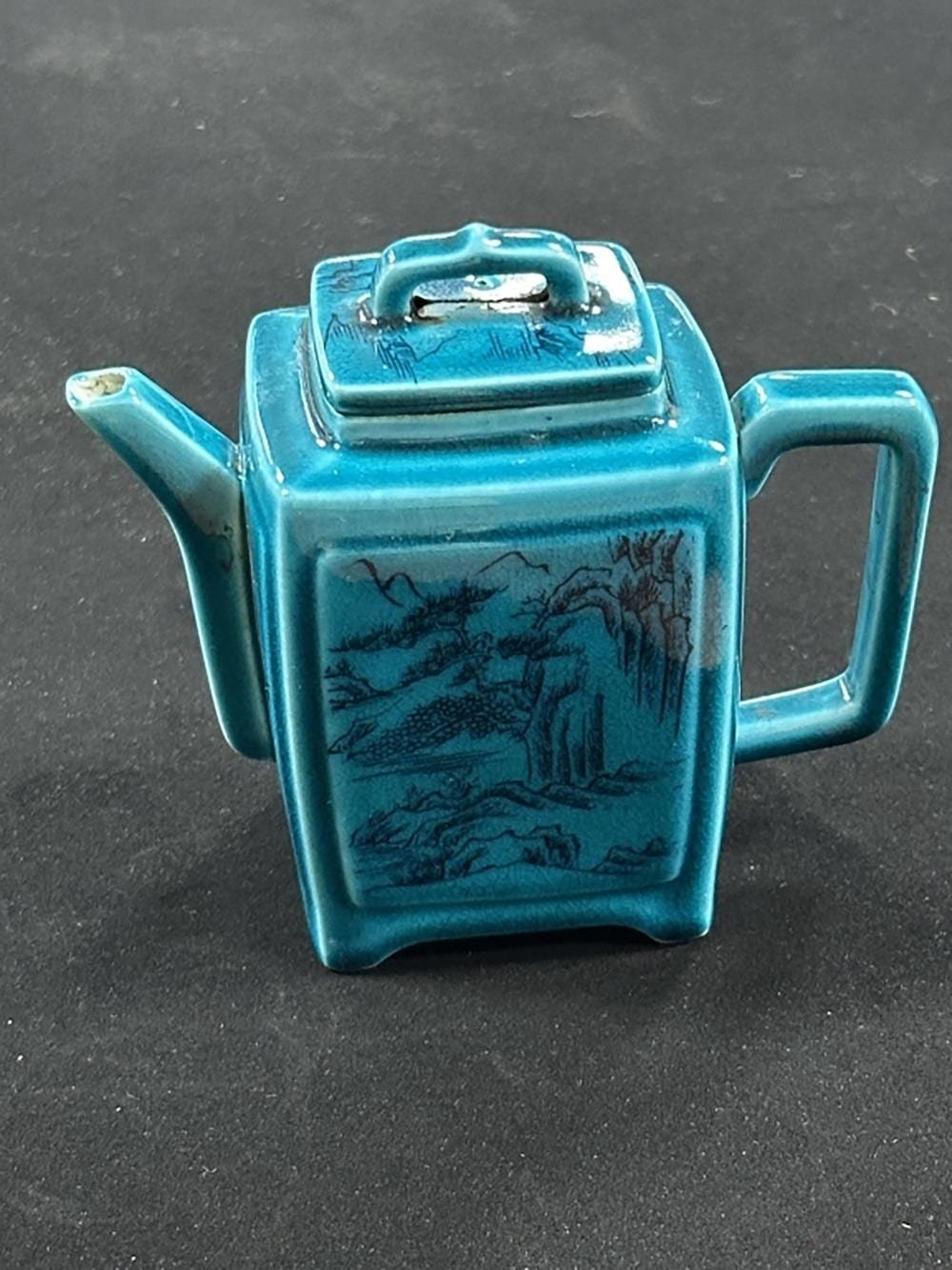 Blue ceramic Chinese-style teapot with a hinged lid and handle, featuring a dark landscape scene on the front.