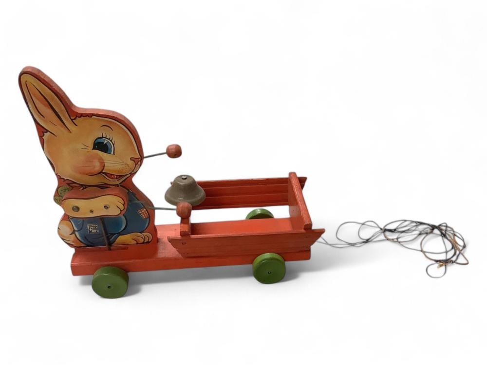 Colorful vintage pull toy of a rabbit riding a red sled on four green wheels with a metal pull handle and a rope trailing behind.