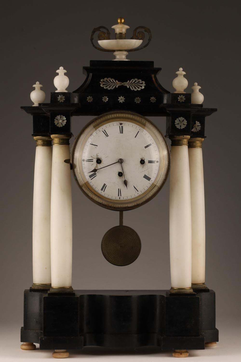 Front view of an antique-style mantel clock with a white dial, black Roman numerals, black case, and white columns with gold accents.