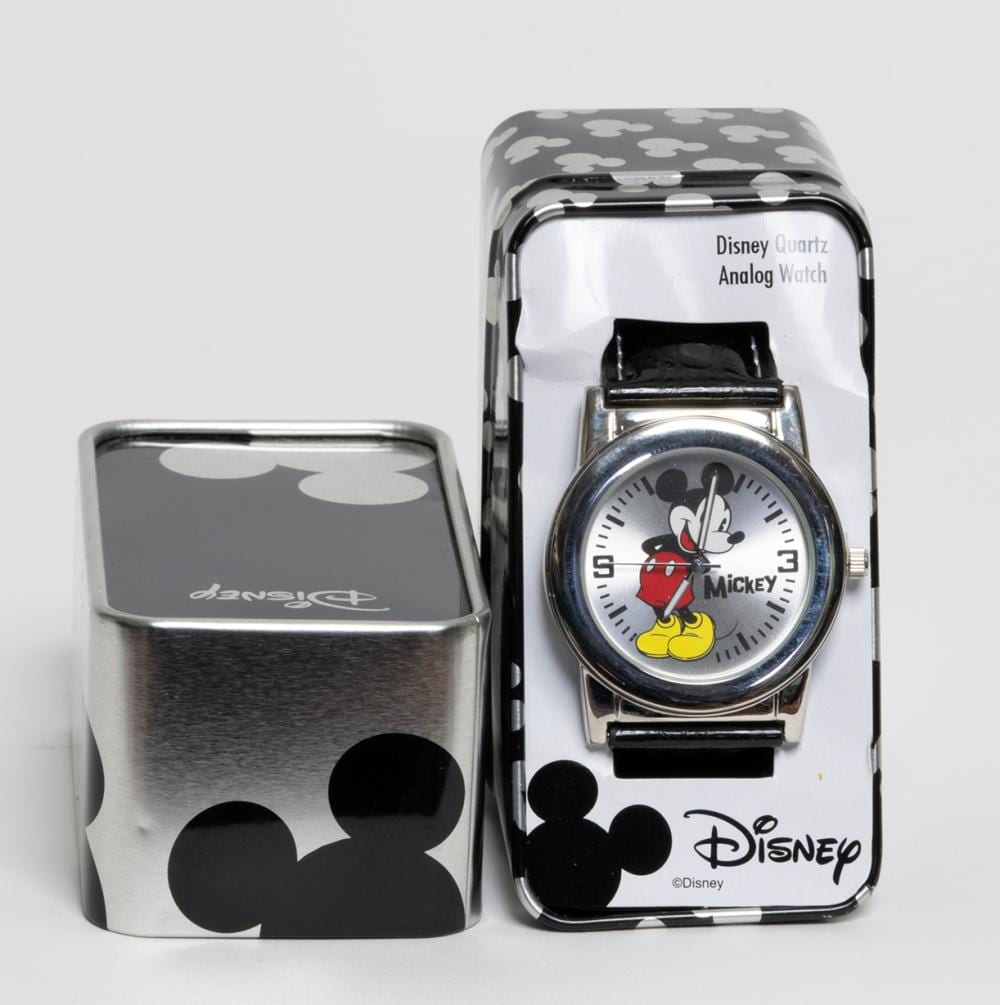 Two Mickey Mouse-themed wristwatches with black and gray patterned faces and cases, one shown open in its plastic packaging.