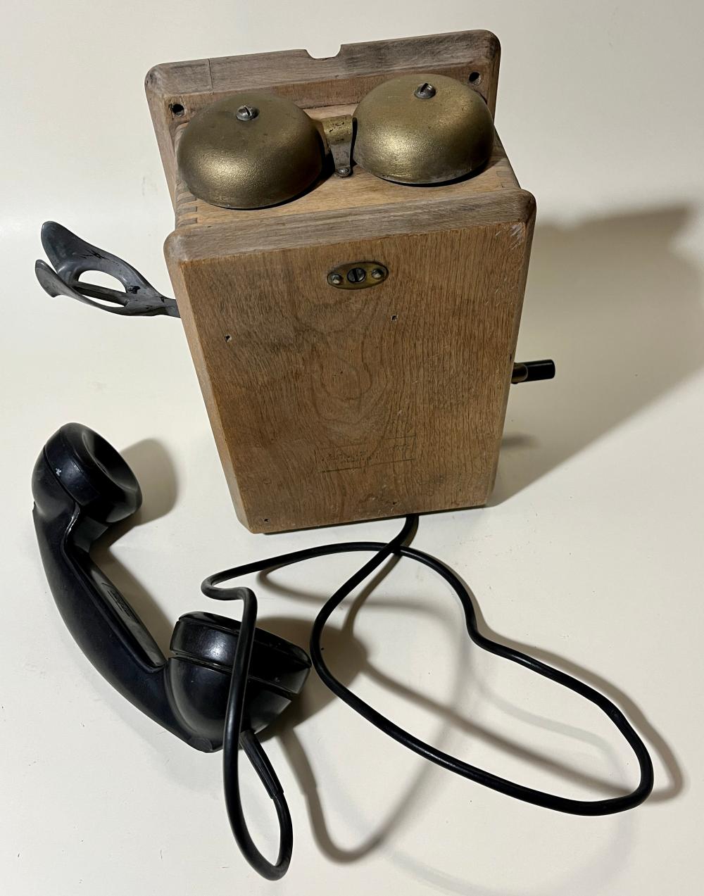 Wooden crank-style telephone base with two metal domed receivers on top and black handset and cord pictured beside it.