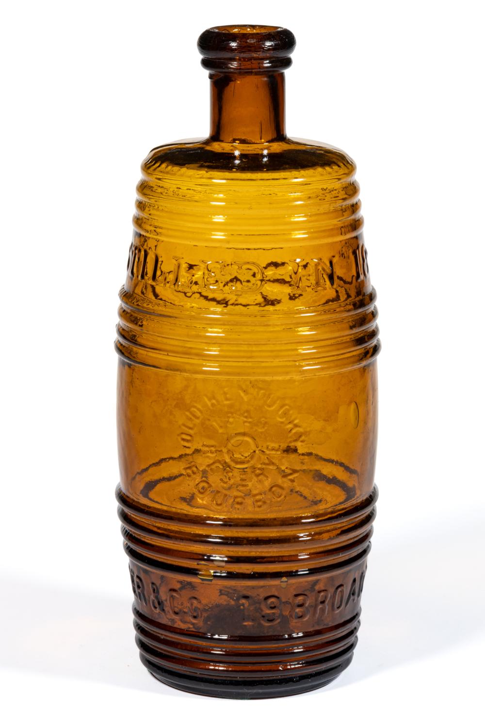 Amber glass barrel-shaped whiskey bottle with a dark rounded stopper top and embossed decorative banding.