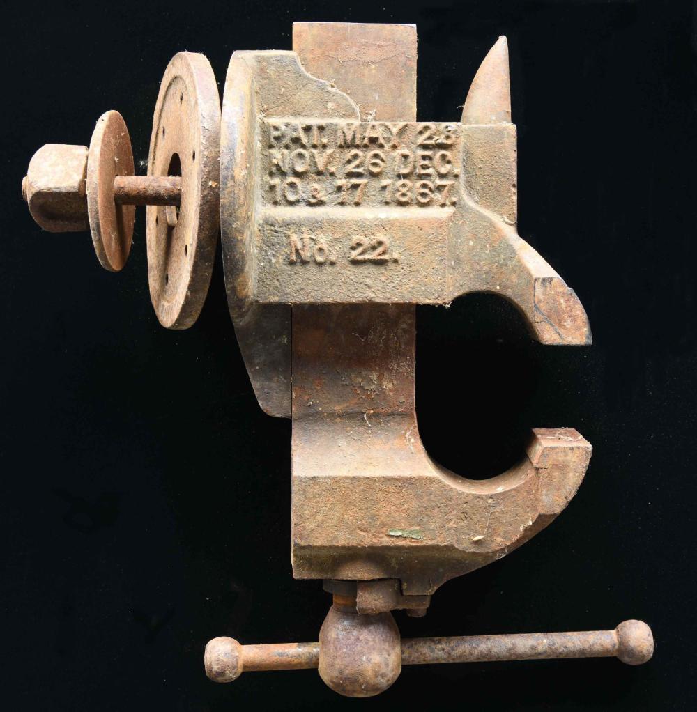 Rusty metal bench vise with a round handle and side jaw, shown against a dark background.