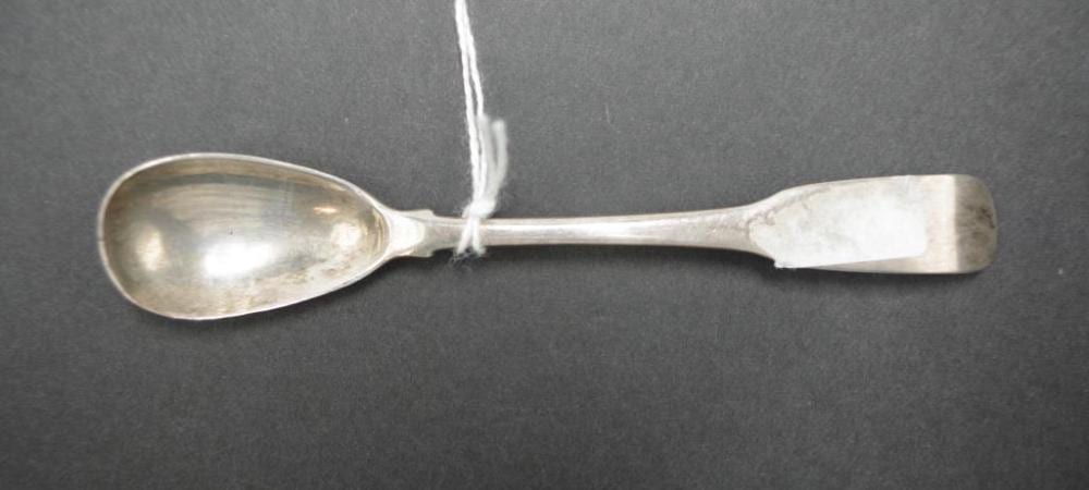 Silver spoon with an oval bowl and long handle, shown on a dark background with a small tag tied near the middle.