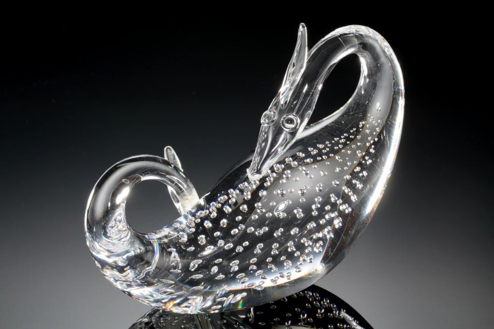 Clear glass dragon figurine with a curved body, raised head, and sparkling dotted pattern across the back, shown on a dark background.
