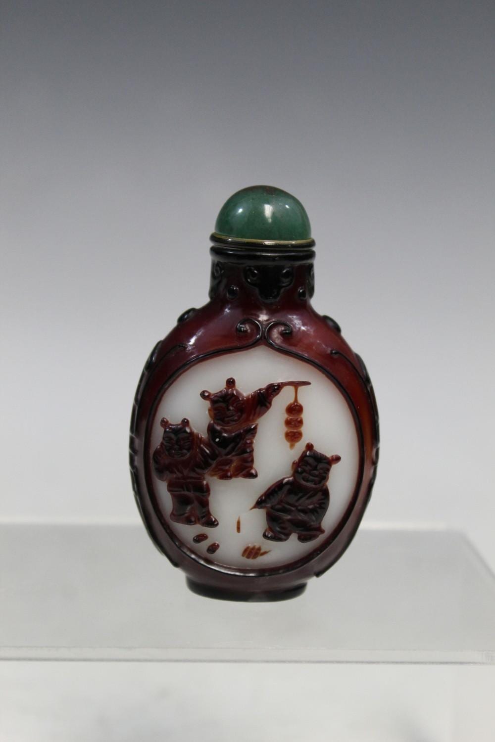 Close-up of a small glass snuff bottle with a green rounded stopper and a dark maroon body decorated with figures on a white panel.