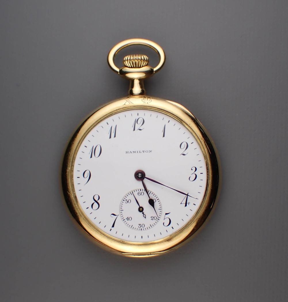 Gold-tone pocket watch with an open face showing a white dial, black numerals, and a small seconds subdial.