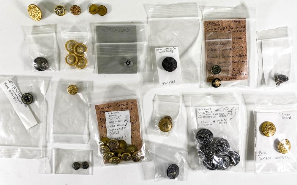 Assorted vintage military-style metal buttons and insignia in individual clear plastic bags on a white background.