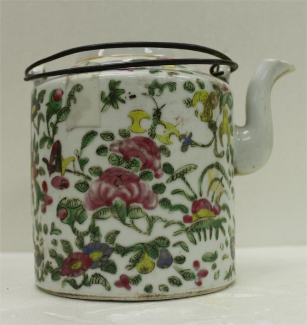 White porcelain teapot with a colorful floral and fruit pattern and a dark metal handle, shown in close-up.