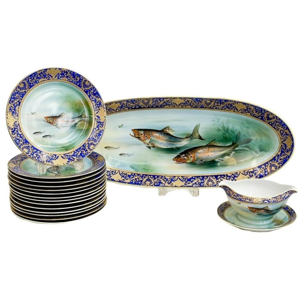 Porcelain tableware set with blue and gold borders, hand-painted fish scene on an oval platter, stacked plates, and a sauce dish with matching decoration.
