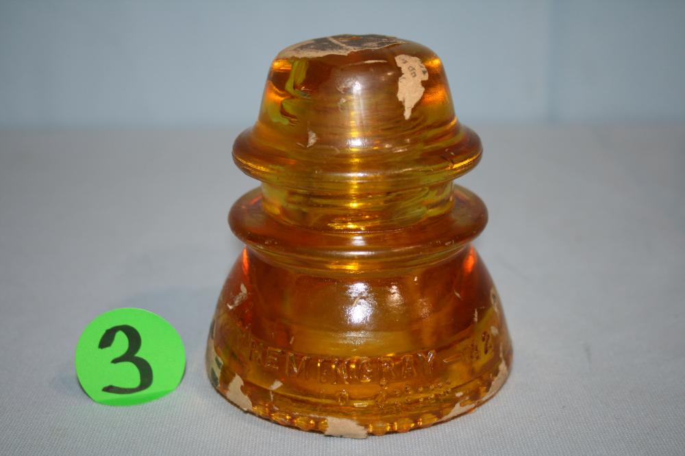 Amber glass electrical insulator with fluted body and ridged dome, photographed on a gray background.