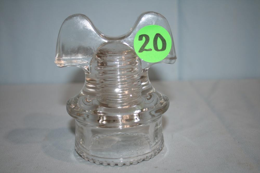 Clear glass insulator with a ribbed center and a green sticker marked “20” on the right side.