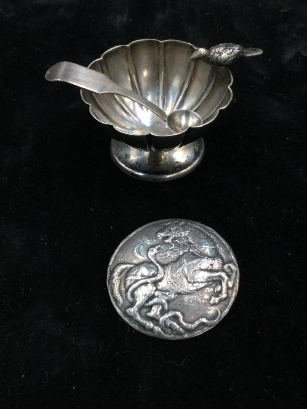 Silver-toned bird-shaped salt cellar with fluted bowl and small spoon-like lid set on a dark background.