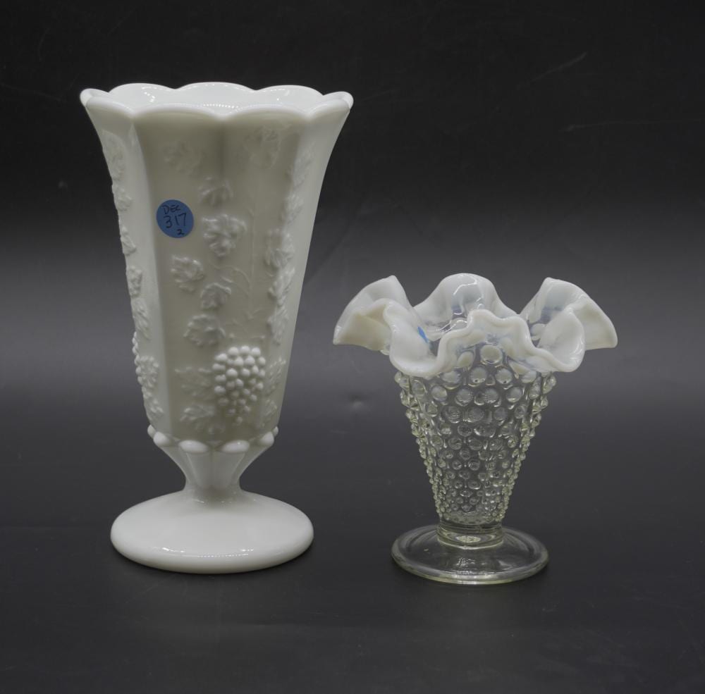 Two white opalescent glass vases on a dark background: a tall fluted vase with raised floral and grape-like pattern, and a smaller clear vase with grape-texture